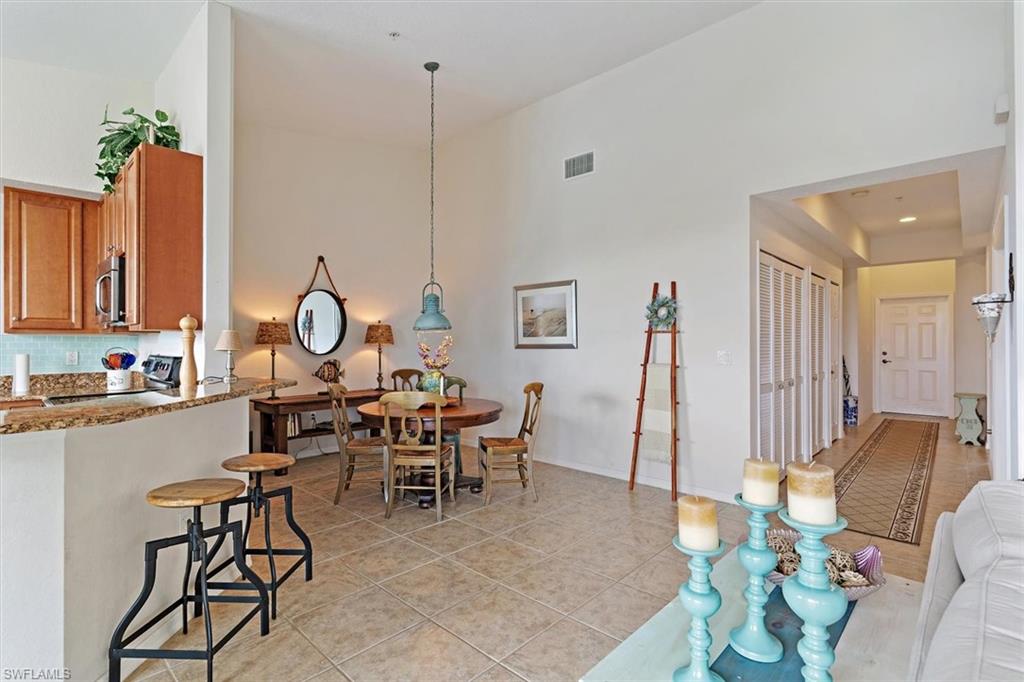 Open-concept living area featuring high vaulted ceilings, tile flooring, a kitchen pass-through with granite countertops, and wood-finish cabinetry