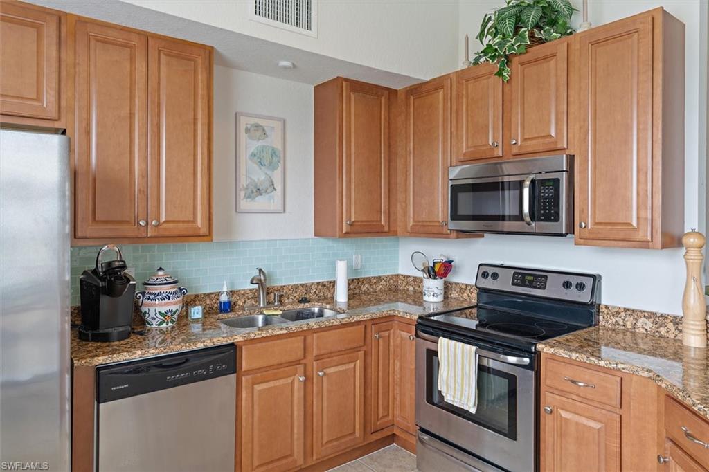 Kitchen featuring light wood cabinetry, a granite-style countertop, a tile backsplash, and stainless steel appliances including a refrigerator, dishwasher, oven, and microwave