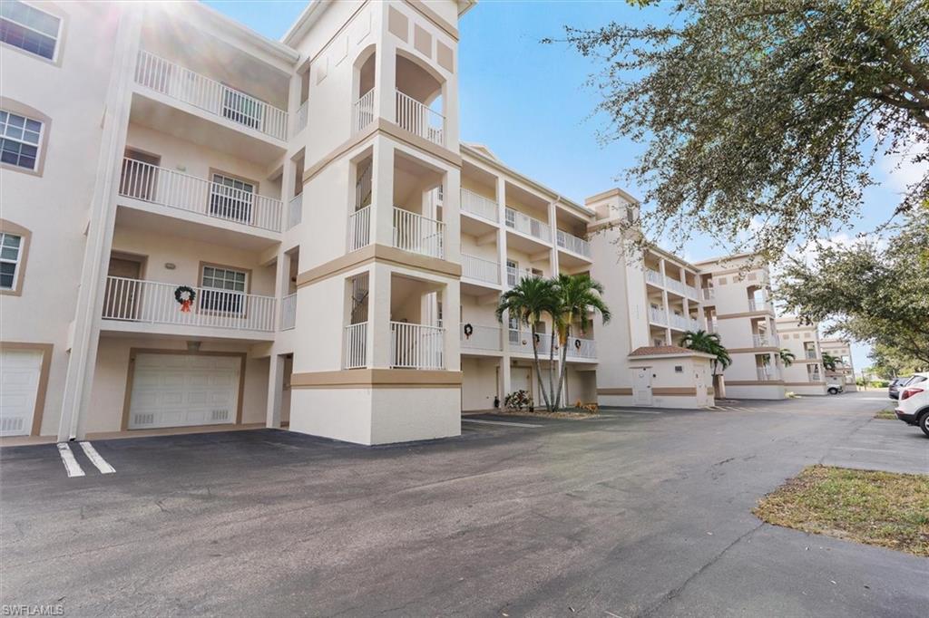 Multi-story stucco exterior featuring individual balconies with white railings, ground-level garages, and mature palm tree landscaping
