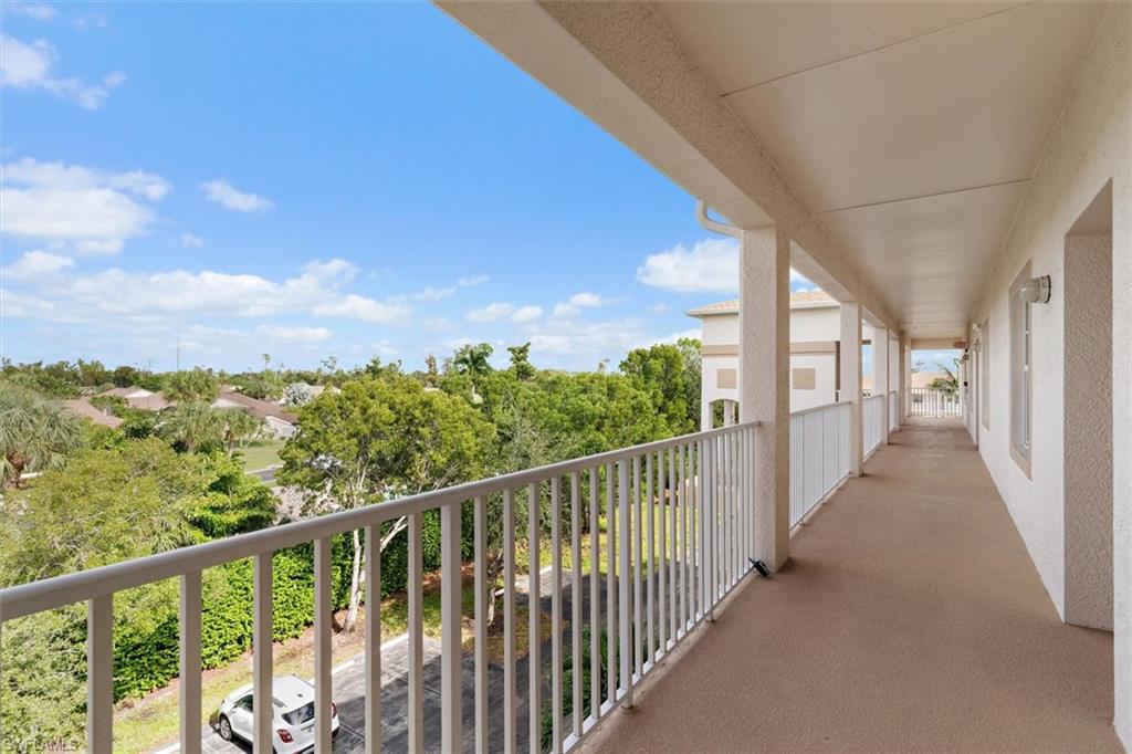 Exterior balcony featuring a concrete floor, white metal railing, textured stucco walls, and a recessed ceiling with wall-mounted light fixtures