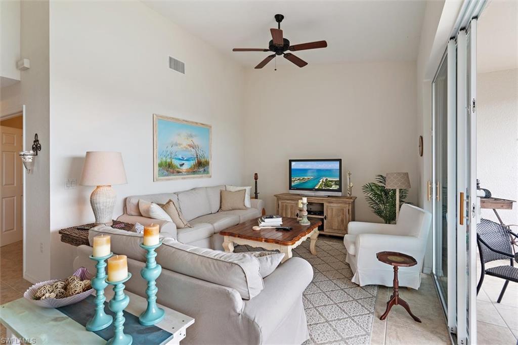 Vaulted ceiling living area featuring light-toned walls, tile flooring, and sliding glass doors opening to the outdoors