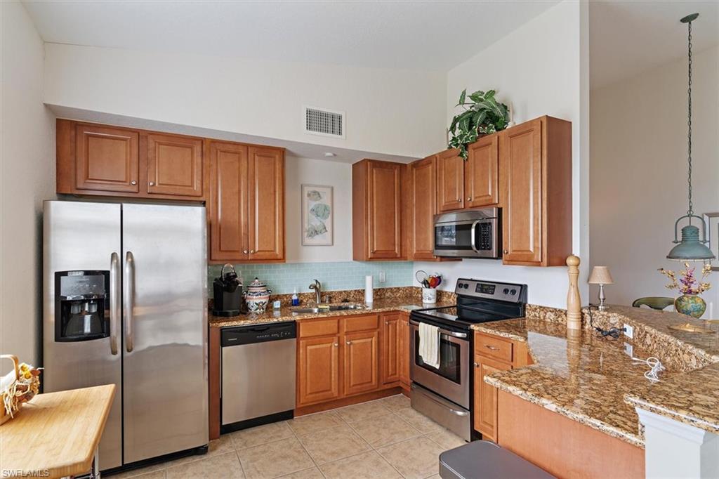 Kitchen featuring wood cabinetry, stainless steel appliances, speckled countertops, a tile backsplash, and tile flooring