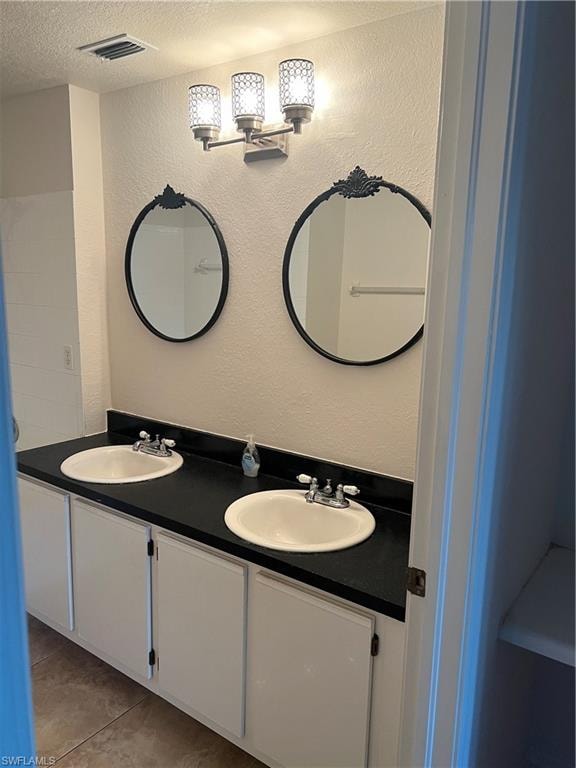 Full bathroom with a textured wall, double vanity, a textured ceiling, and light tile patterned floors