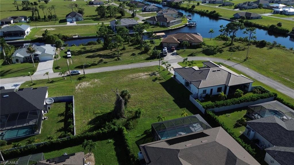 Aerial view showcasing expansive manicured grounds with mature landscaping, multiple residences featuring dark-roofed architecture, and serene waterfront access visible in the distance across this spacious residential community setting