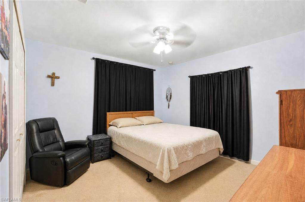 Virtually Staged Carpeted bedroom featuring light blue walls, a ceiling fan with integrated lighting, and two windows with dark privacy drapes