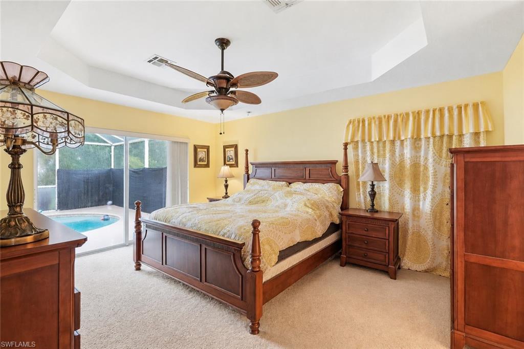 Virtually Staged Tray ceiling with a ceiling fan, carpeted flooring, and sliding glass doors opening to a screened pool area