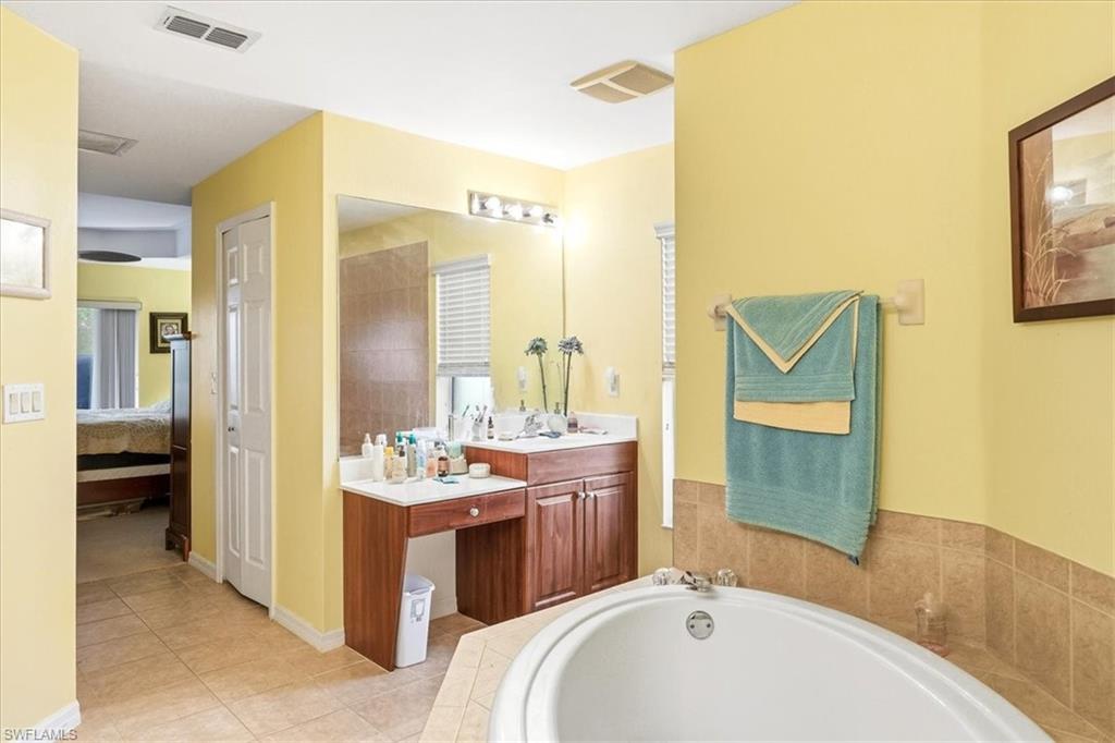 Bathroom featuring a built-in corner soaking tub, a dual-sink vanity with a dedicated seated area, a large wall-mounted mirror, and tile flooring