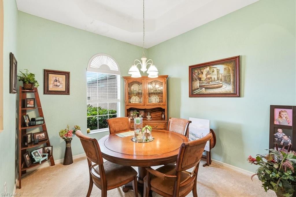 Carpeted dining area featuring a wood-finish round table and chairs, arched window with blinds, wood-finish china cabinet, and suspended chandelier