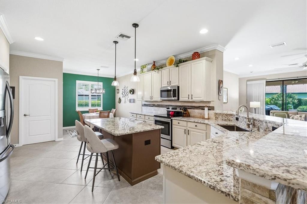 Spacious kitchen featuring light-toned cabinetry, granite countertops, stainless steel appliances, a large center island with pendant lighting, and tile flooring