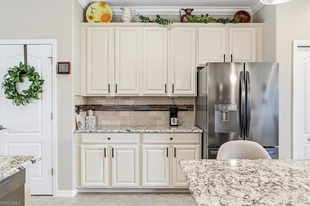Kitchen featuring cream cabinetry with black hardware, a stainless steel French door refrigerator, speckled granite countertops, and a tiled backsplash with decorative accents