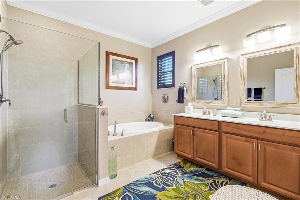 Bathroom featuring a glass-enclosed shower, built-in soaking tub, dual vanity with wood-finish cabinetry, white countertops, and individual framed mirrors