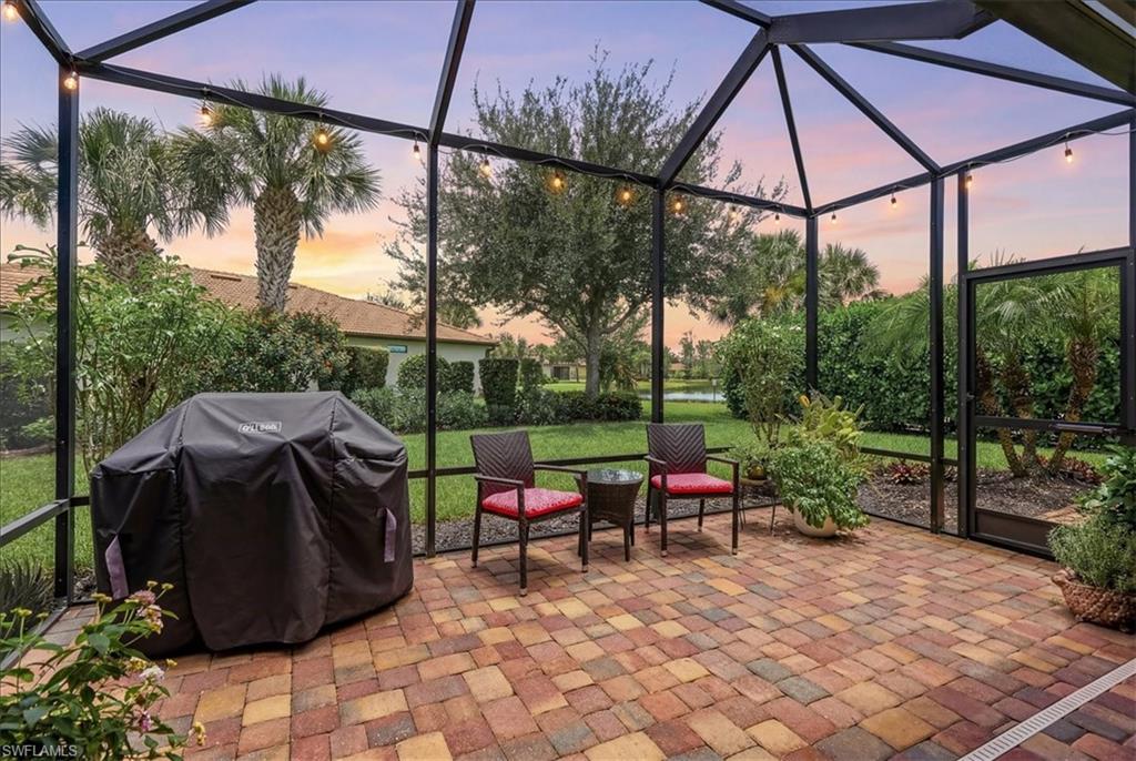 Screened patio featuring multicolor paver flooring, string lighting, and direct access to the landscaped yard