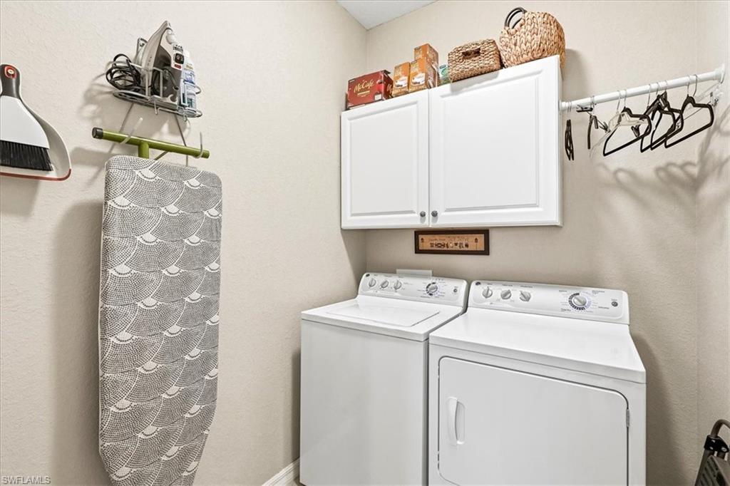 Dedicated utility space featuring a washer and dryer, upper cabinetry, and a wall-mounted drying rack