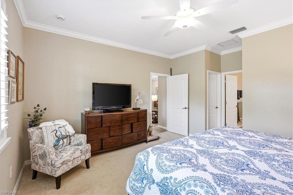 Interior room featuring crown molding, neutral wall tones, carpeted flooring, a ceiling fan with integrated lighting, and multiple interior doorways