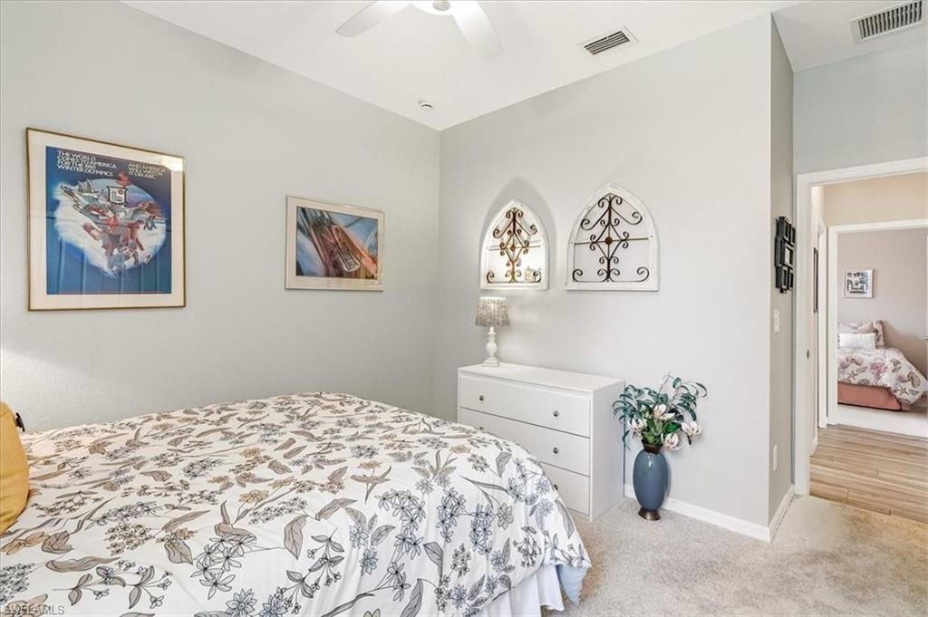 Carpeted interior room with light gray walls, a white ceiling fan, and architectural wall decor