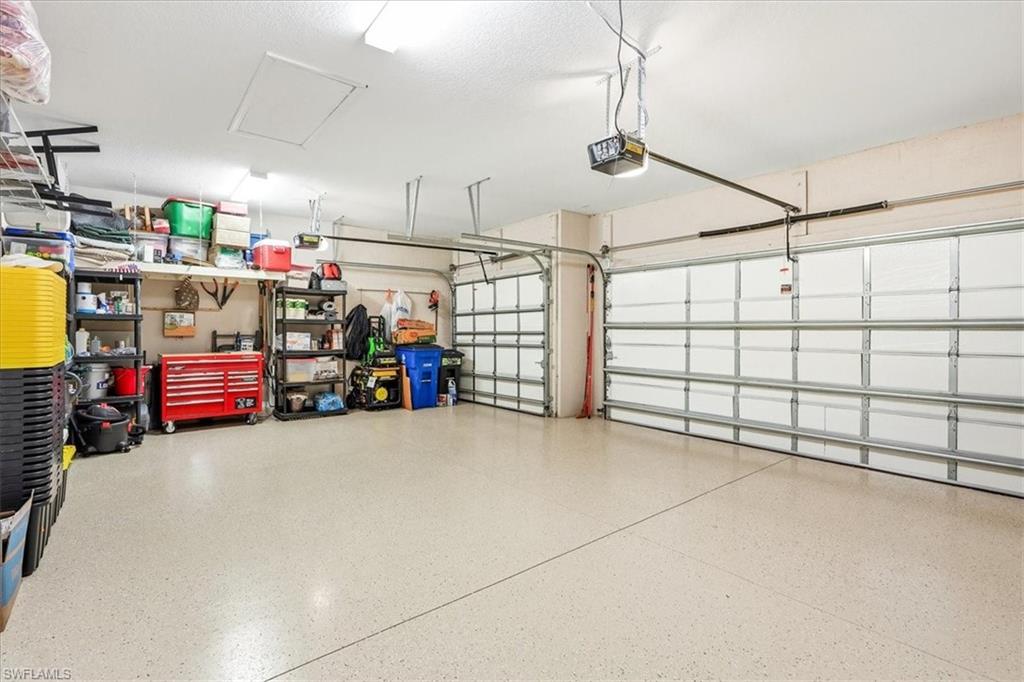 Spacious garage featuring a light-toned, speckled epoxy floor, two overhead garage doors, and built-in shelving