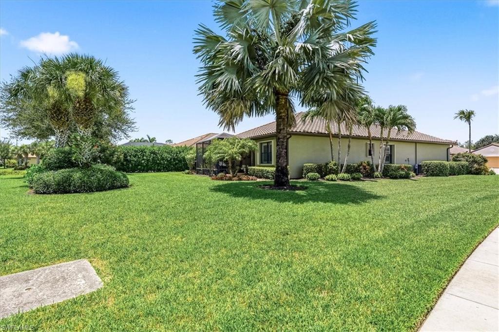 Expansive lawn with mature palm trees and established landscaping bordering a one-story property with a tile roof and stucco exterior