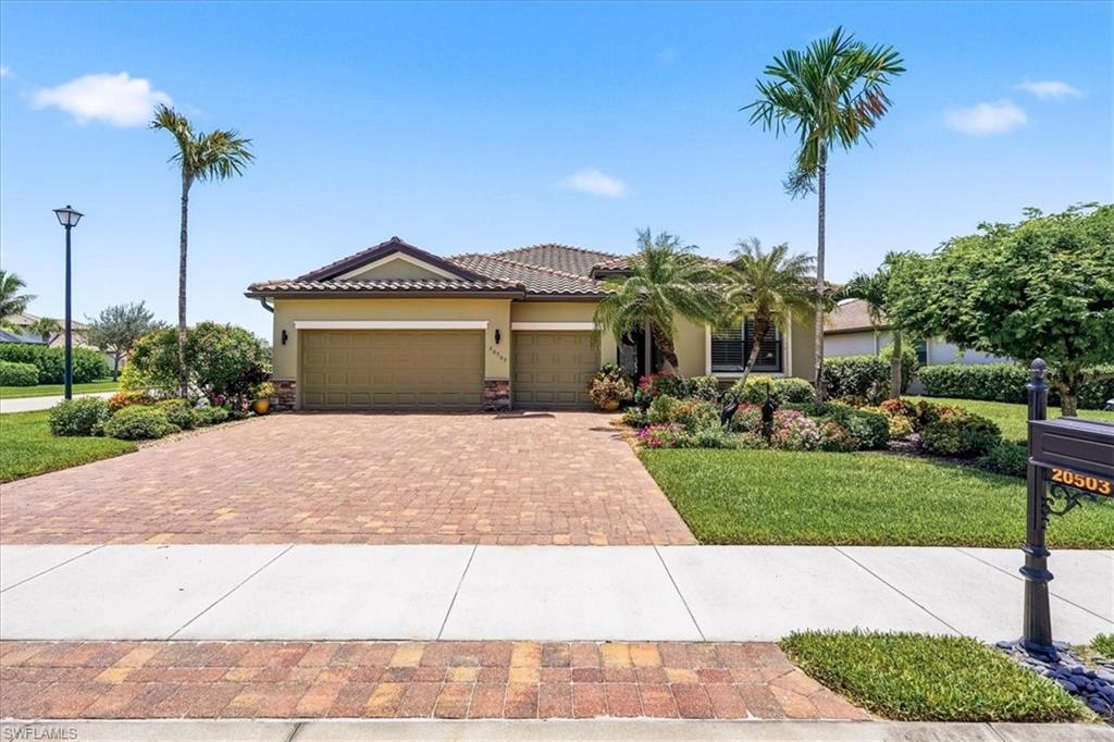 Exterior featuring a paver driveway, two-car garage, Mediterranean tile roof, and mature palm trees