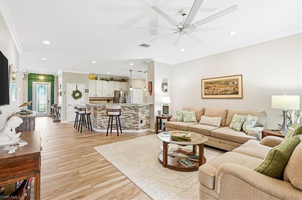 Open-concept living space featuring wood-look tile flooring, crown molding, a ceiling fan, recessed lighting, and a stone-clad breakfast bar with pendant lighting
