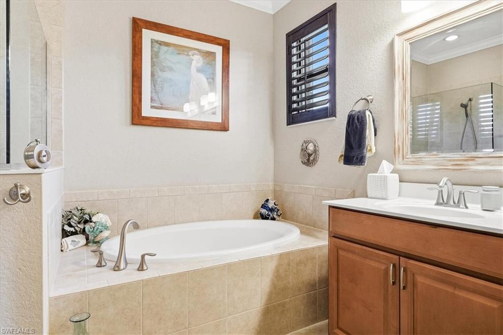 Built-in soaking tub with tile surround, wood-finish vanity with single sink, framed mirror, and a glass-enclosed shower