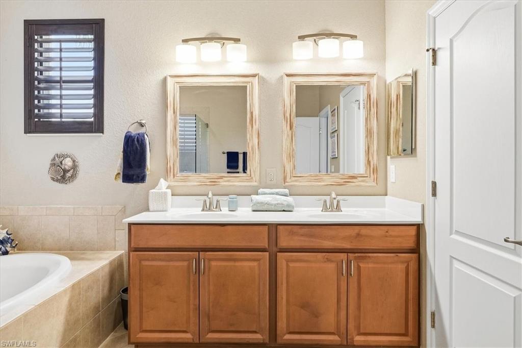 Dual wood-finish vanities with white countertops and undermount sinks, illuminated by individual three-light fixtures