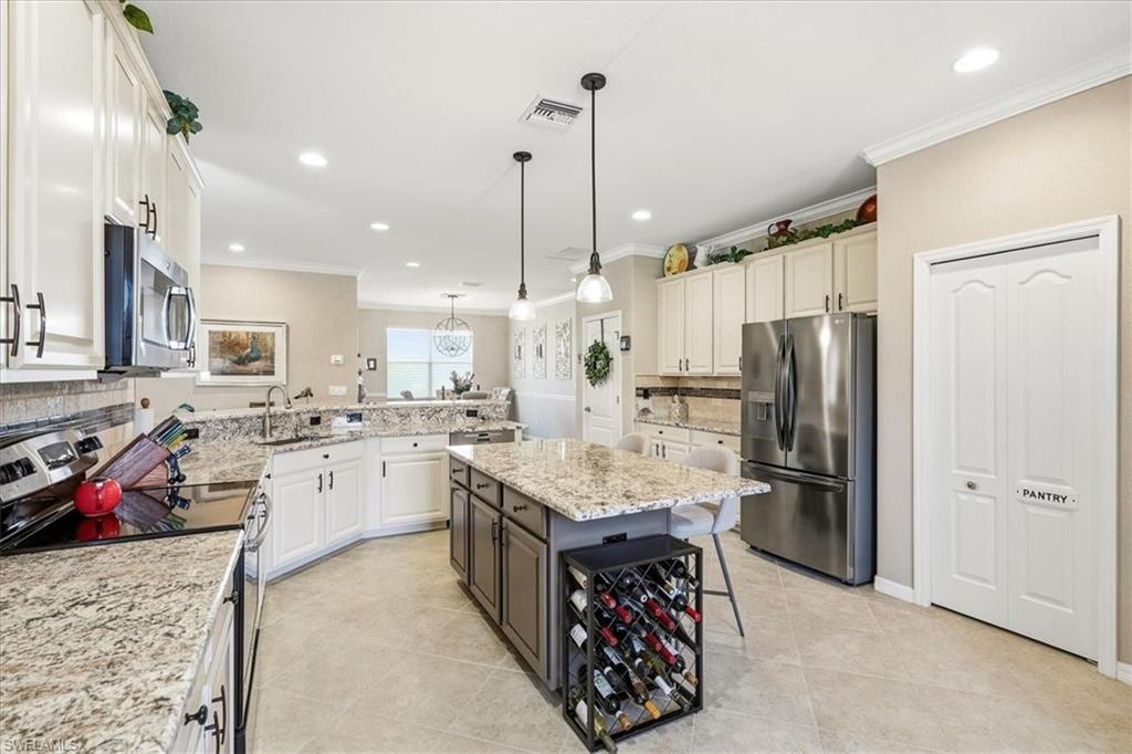 Spacious kitchen featuring light-toned cabinetry, stainless steel appliances, granite countertops, tile flooring, and a central island with pendant lighting