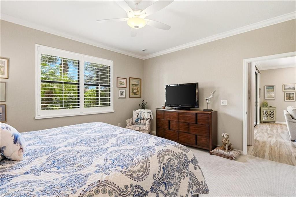 Bedroom featuring a large window with plantation shutters, neutral wall paint, white crown molding, and a ceiling fan with integrated lighting