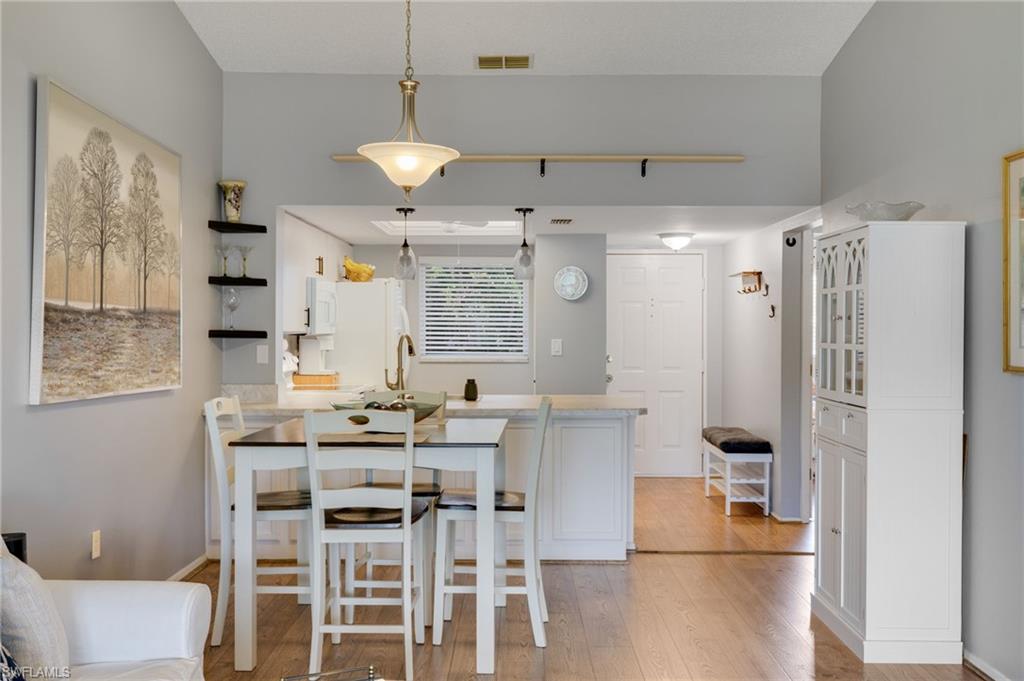 Open-concept living space featuring wood-finish flooring, a kitchen island with seating, pendant lighting, and vaulted ceilings