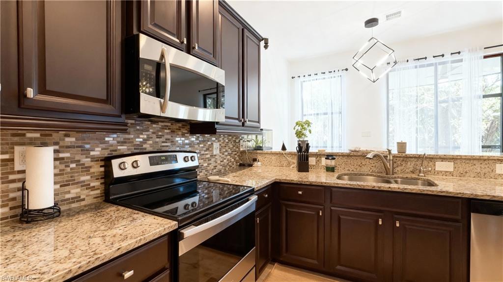 Kitchen with stainless steel appliances, tasteful backsplash, dark brown cabinetry, and light stone counters