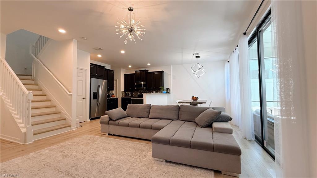 Living room with stairway, a chandelier, light wood-type flooring, and recessed lighting