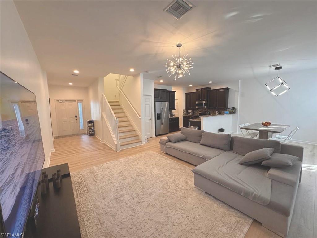 Living room featuring stairway, a chandelier, recessed lighting, and light wood finished floors