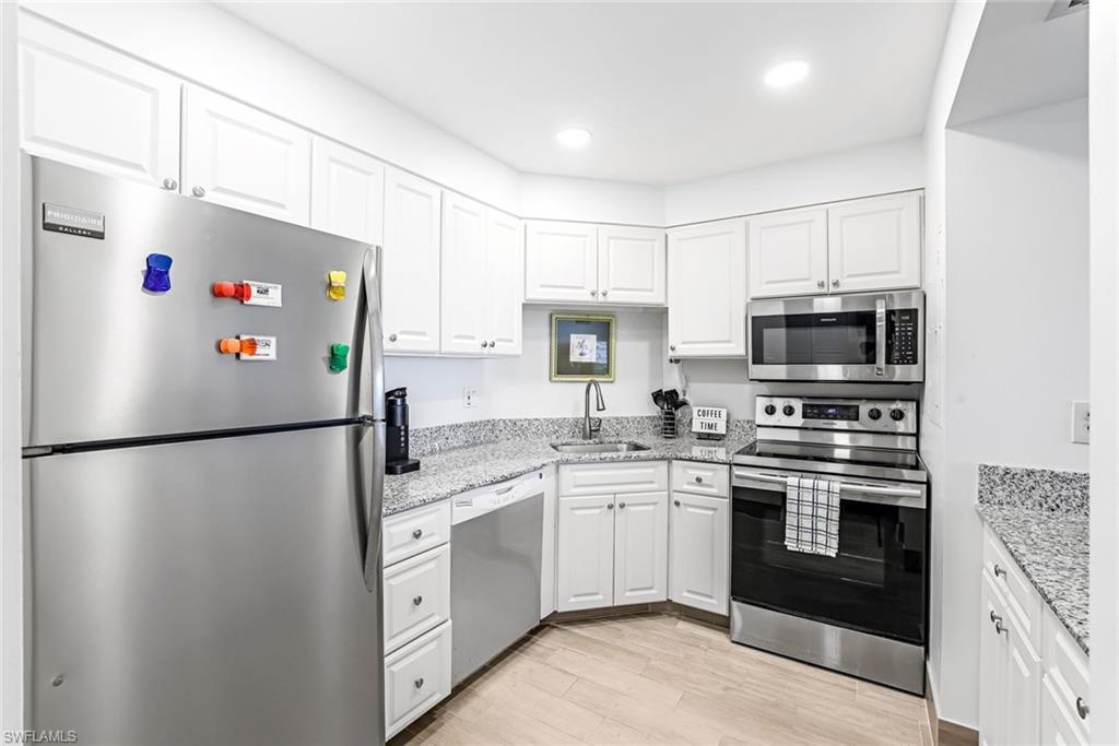 Kitchen with stainless steel appliances, light hardwood / wood-style flooring, white cabinets, and sink