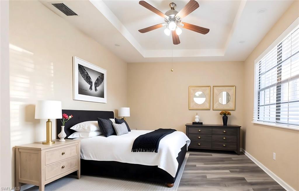 Bedroom featuring wood finished floors, a raised ceiling, and a ceiling fan