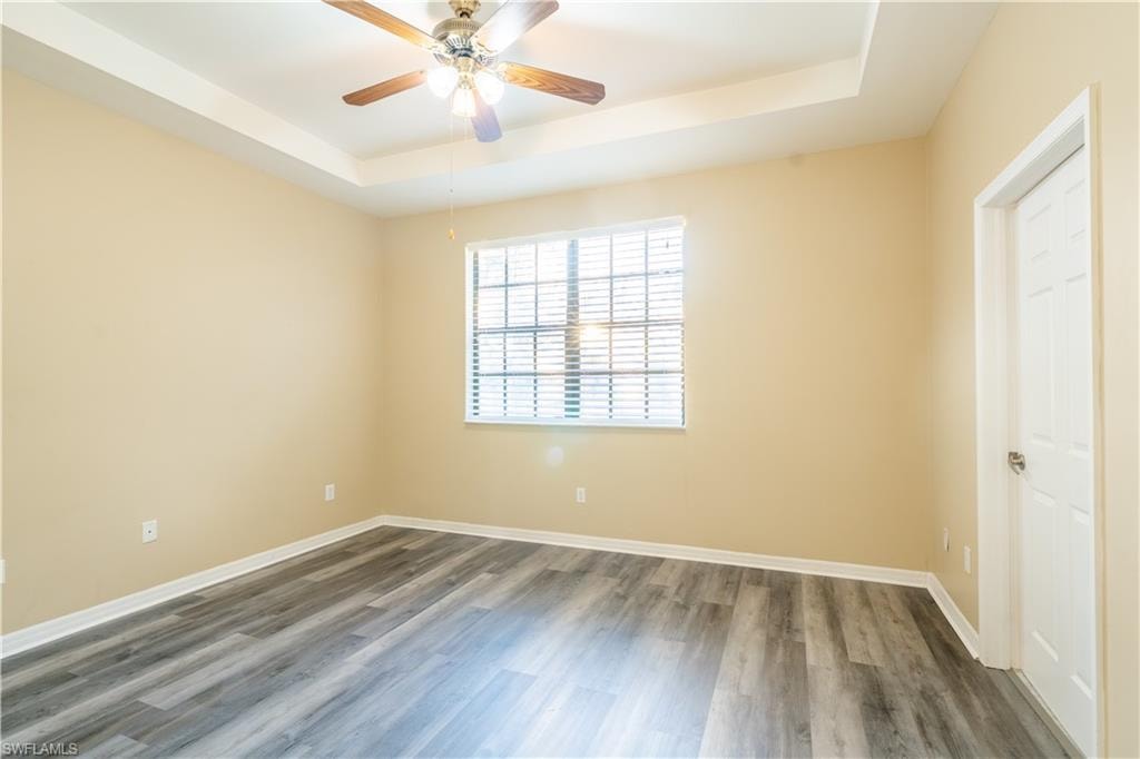 Empty room featuring a raised ceiling, wood finished floors, and a ceiling fan