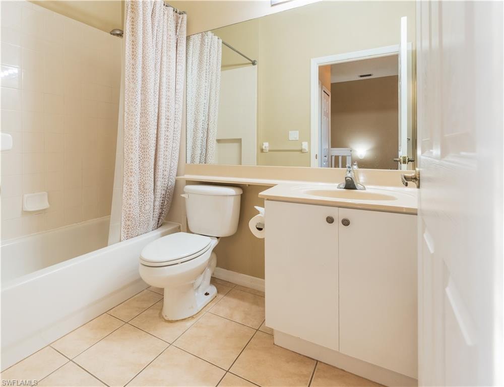 Full bath with vanity, shower / bath combo with shower curtain, and light tile patterned floors