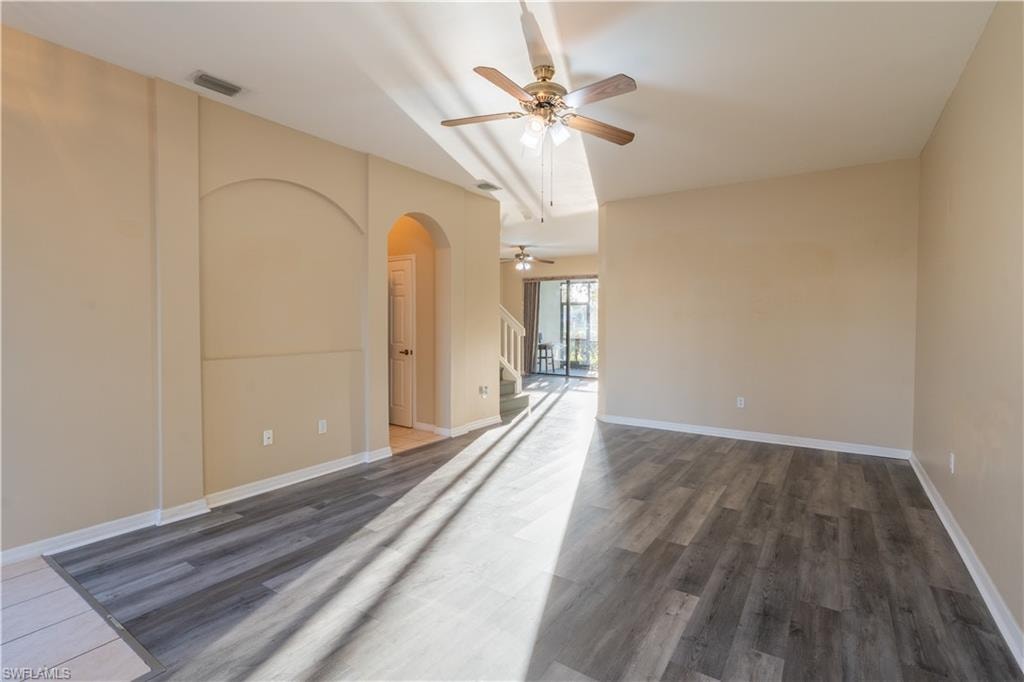 Unfurnished room featuring a ceiling fan, dark wood finished floors, and arched walkways