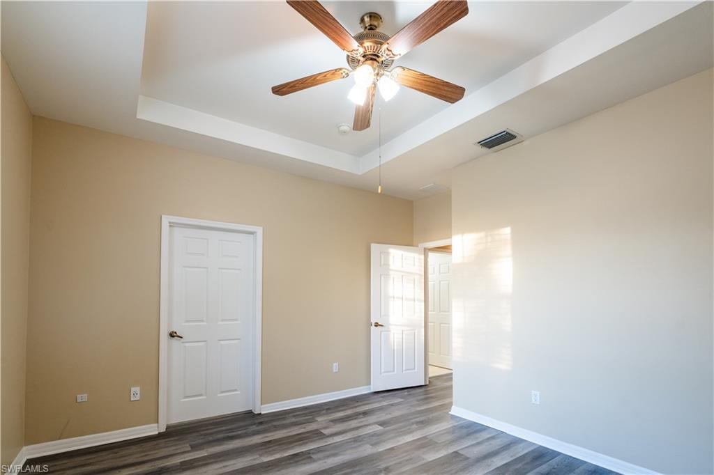Unfurnished bedroom with a tray ceiling, a ceiling fan, and wood finished floors