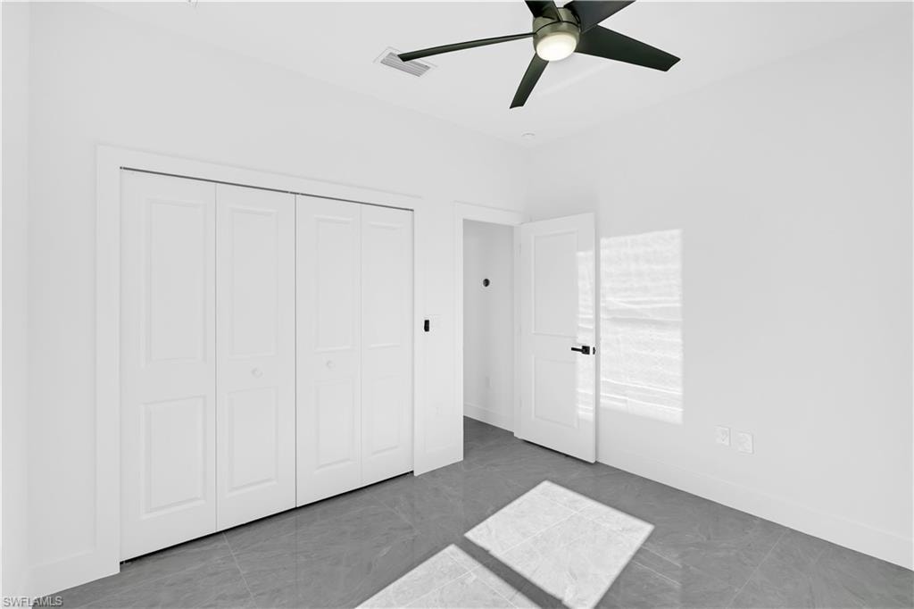 Bright room featuring white walls, gray tile flooring, a modern ceiling fan with integrated lighting, and white bi-fold closet doors