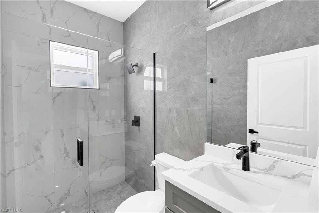 Modern guest bathroom featuring a walk-in shower with clear glass enclosure, large format stone-look wall tiles, and a window