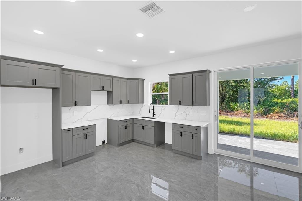Kitchen featuring grey shaker-style cabinetry, white countertops with veining, a white backsplash, and a matte black faucet