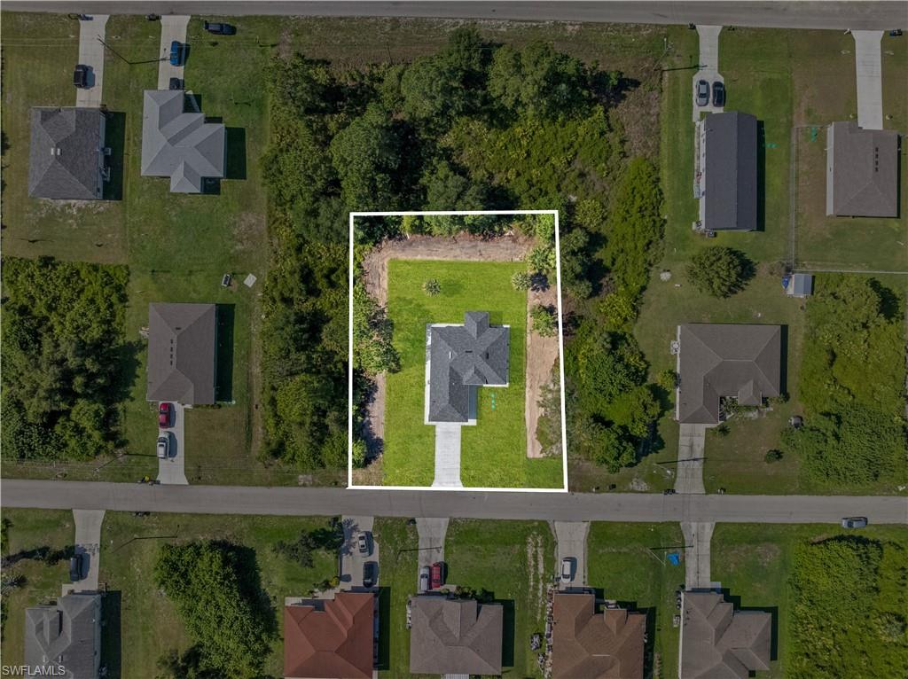 Aerial view showcasing a property with a distinct, newly built home, a manicured lawn, and a paved driveway