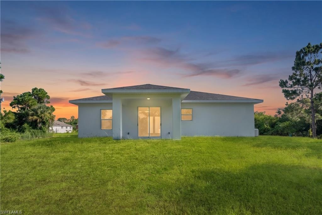Rear exterior featuring a covered patio, sliding glass door entry, multiple windows, and a expansive lawn