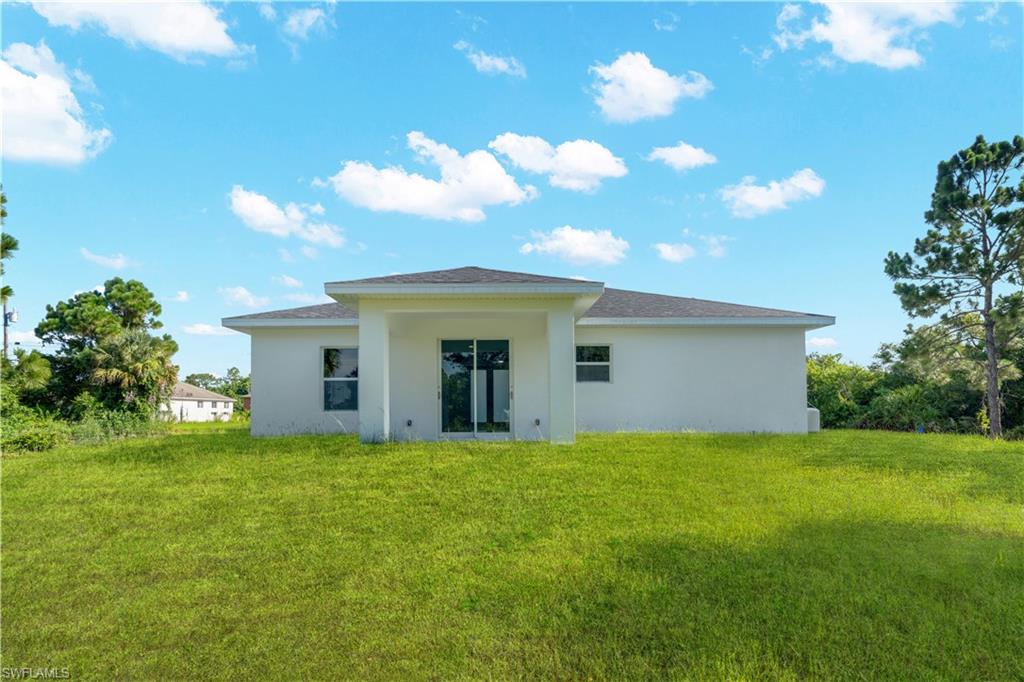 Rear exterior featuring a covered patio with sliding glass doors, white stucco finish, and a dark shingle roof