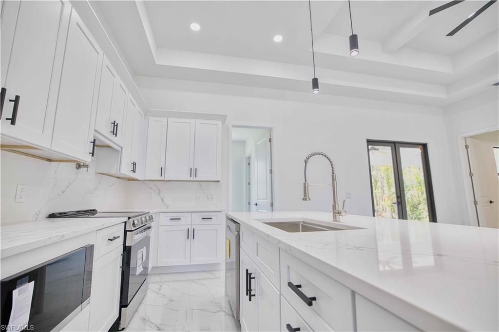 Modern kitchen featuring white cabinetry with matte black hardware, stainless steel appliances, and a large island with an integrated sink