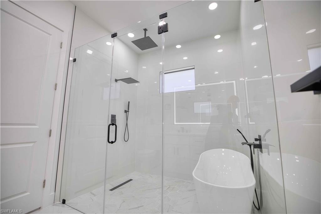 Contemporary bathroom featuring a frameless glass shower enclosure, a freestanding soaking tub with a floor-mounted matte black faucet, and hexagon tile flooring