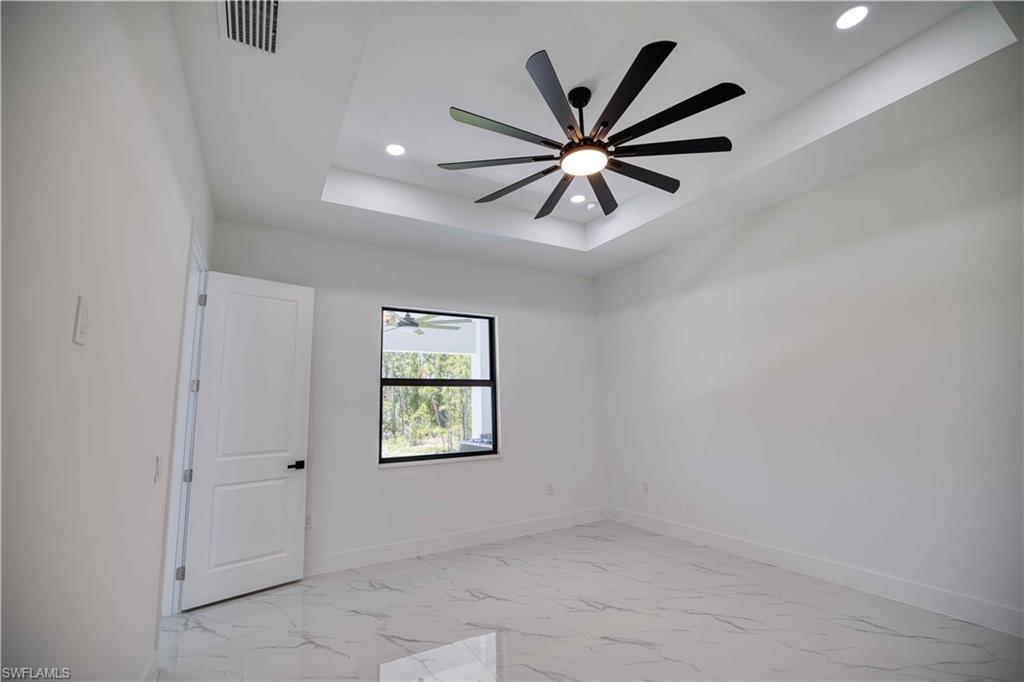 Tray ceiling with a modern ceiling fan and recessed lighting, white walls, and a window with a black frame
