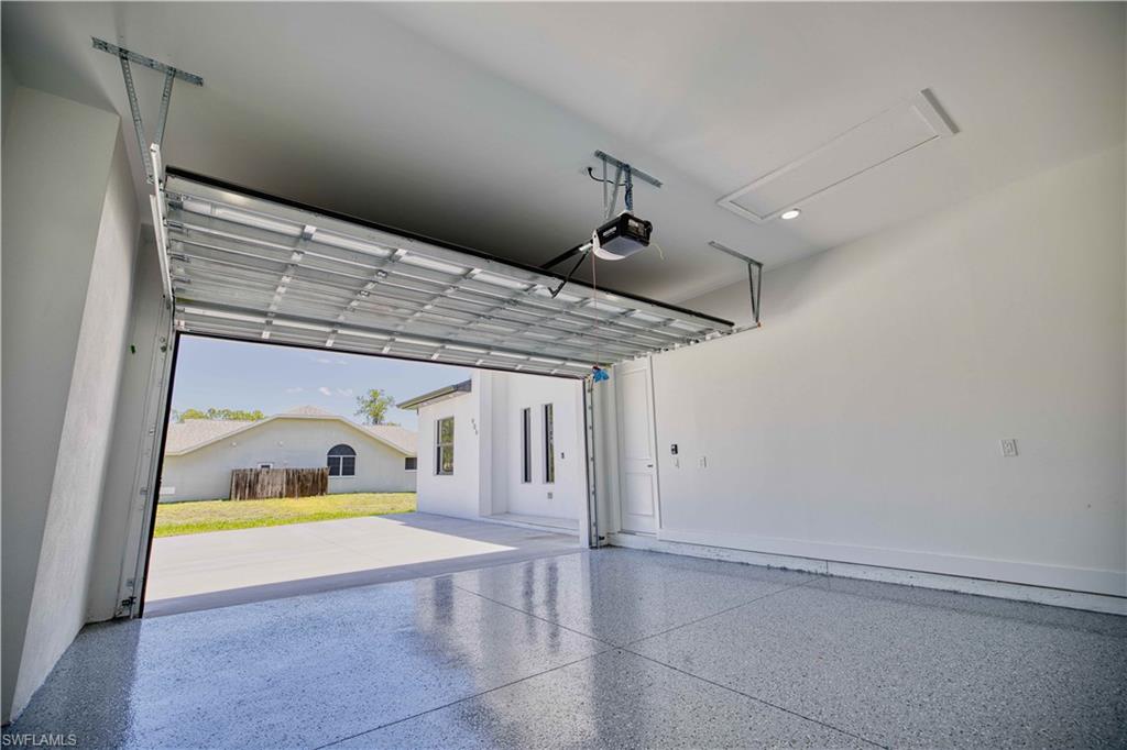 Spacious garage with an epoxy-coated concrete floor, an overhead garage door opener, and a ceiling-mounted access panel