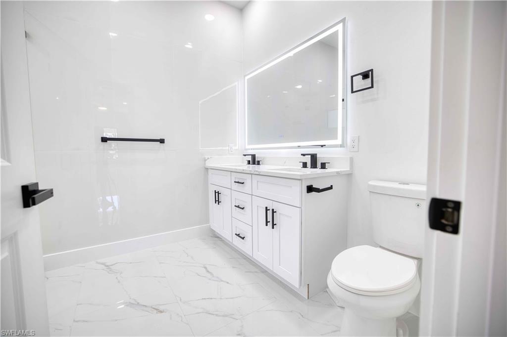 Contemporary bathroom featuring a dual vanity with white cabinetry, black hardware, and a lighted mirror