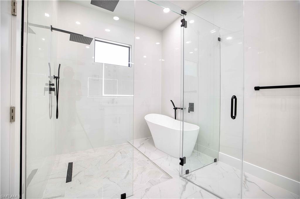 Contemporary bathroom featuring a spacious glass-enclosed shower, freestanding bathtub, rainfall showerhead, matte black fixtures, and marble-look tile flooring