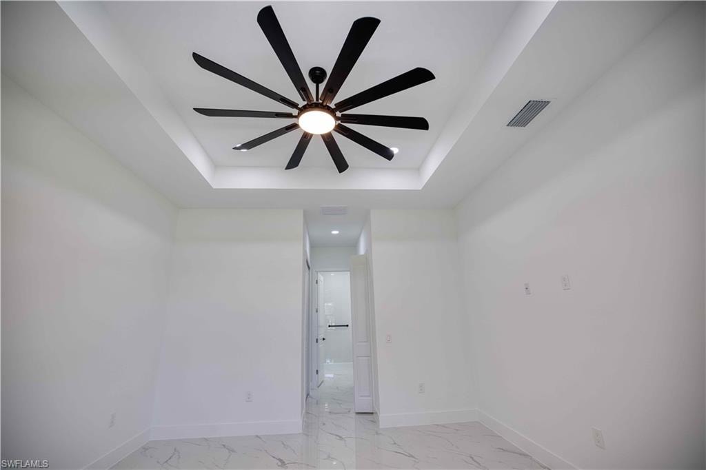Recessed ceiling feature with a large multi-blade ceiling fan, pristine white walls, and marble-look tile flooring